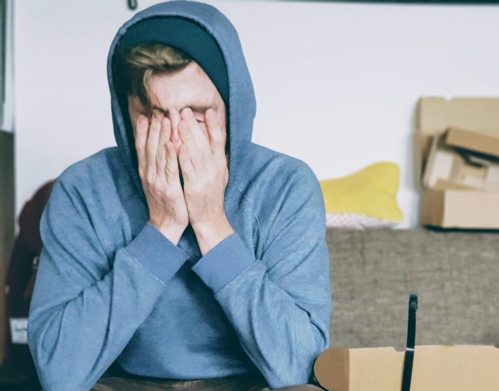 A young man with a hoodie on placing his hands over his face.
