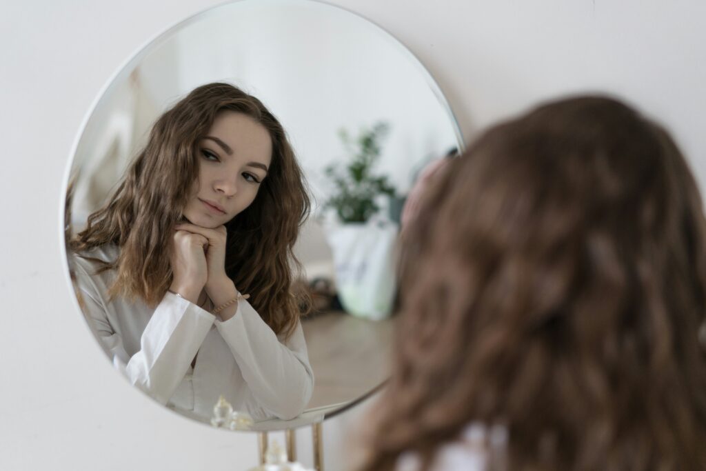 A woman looking at herself in the mirror with her hands on her chin.